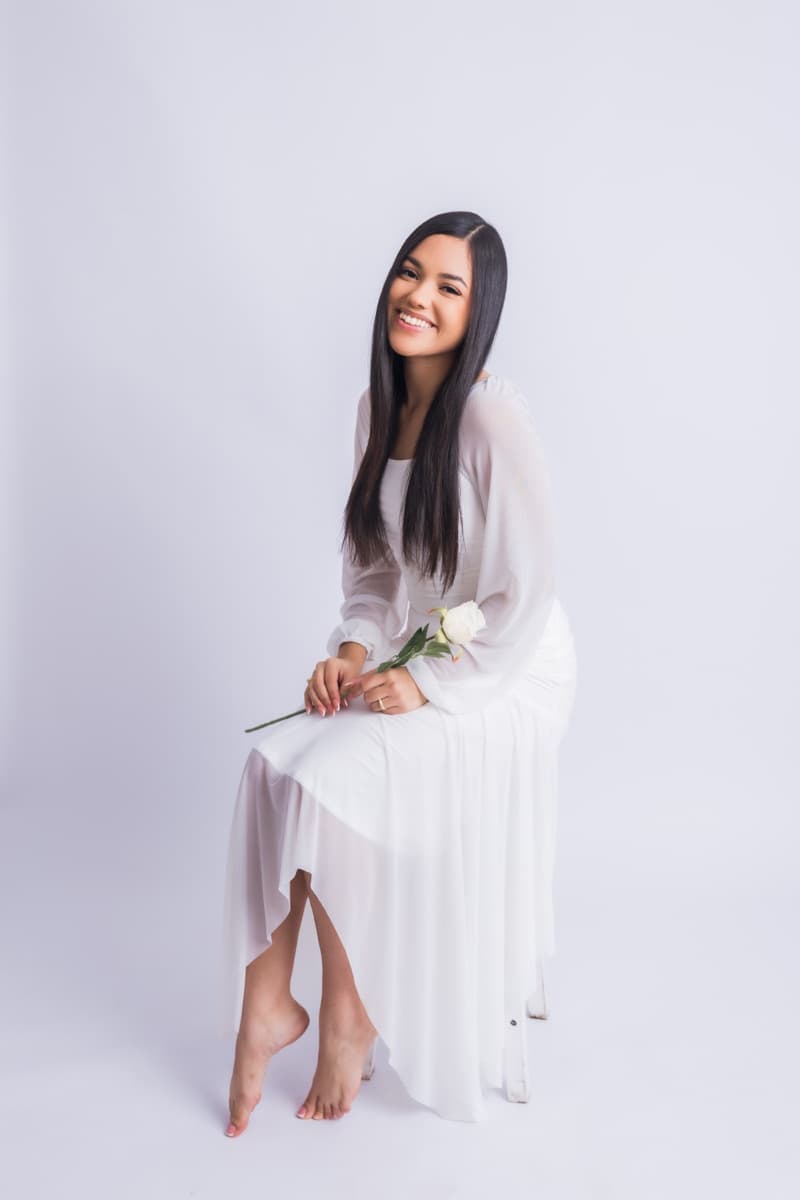 Elizabet Maria sentada, con vestido blanco, sosteniendo una rosa blanca