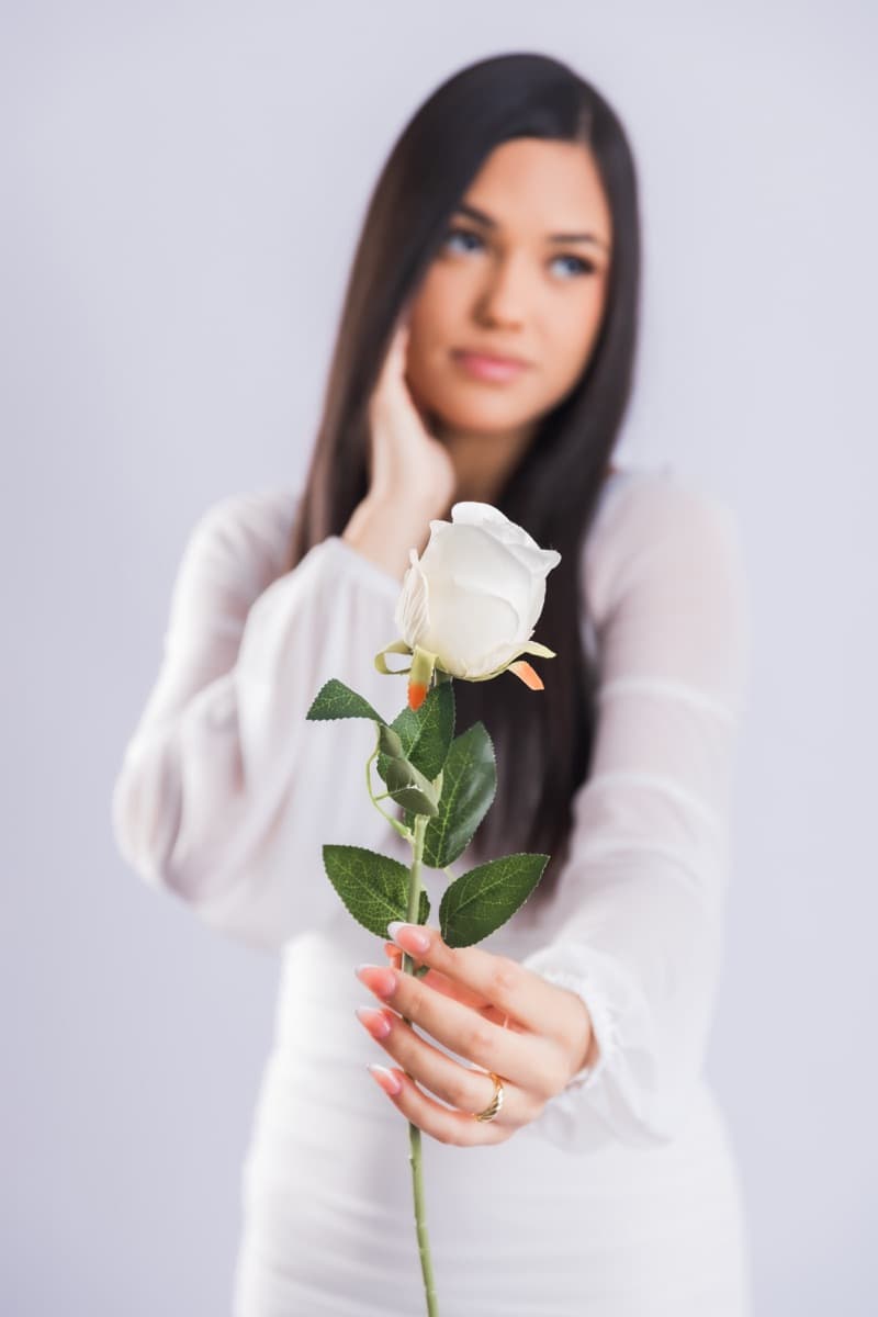 Elizabet Maria con blusa blanca, sosteniendo una rosa blanca junto al rostro