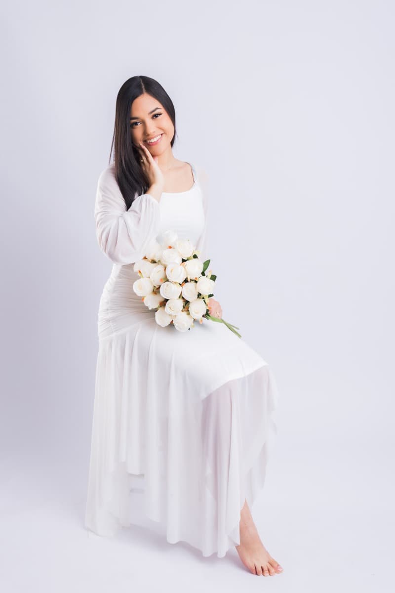 Elizabet Maria sentada, con vestido blanco, con un ramo de rosas blancas
